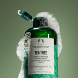 Green bottle of The Body Shop Tea Tree Skin Clearing Facial Wash with soap bubbles on a green background