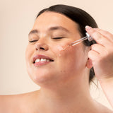 A woman applying The Body Shop Vitamin C Glow Serum to her face
