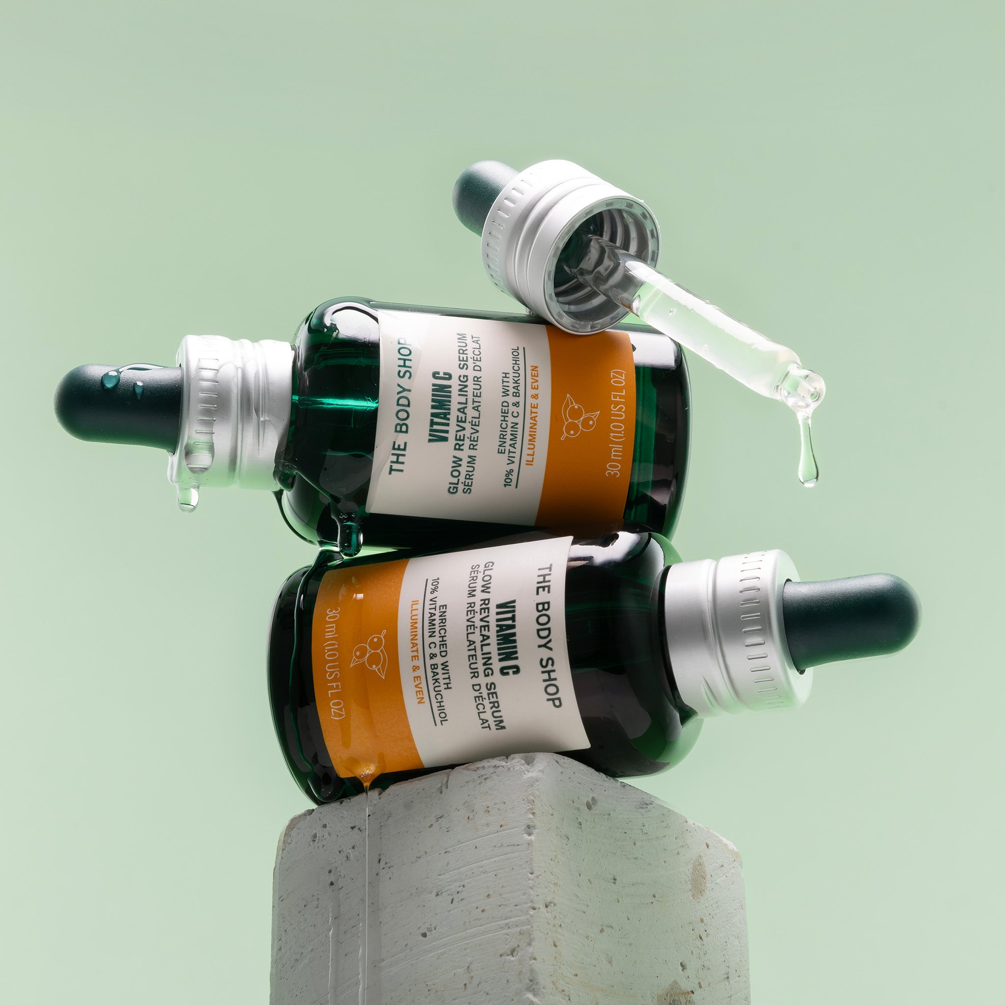 Two Vitamin C Glow Serum bottles on their side, stacked on top of one another, perched on a stone block.