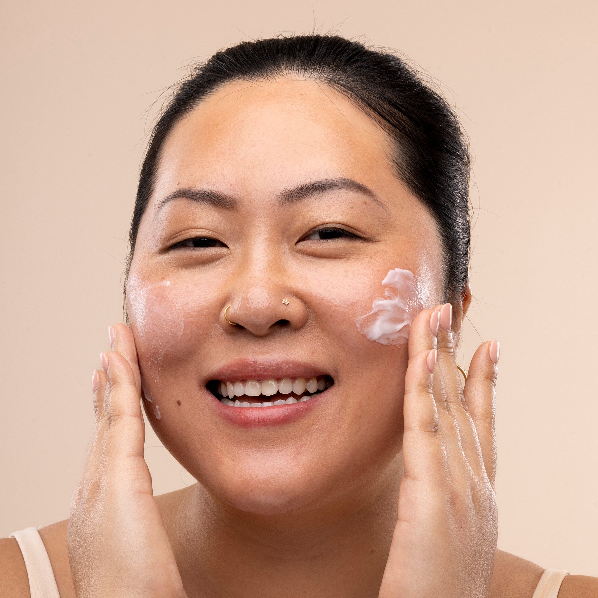 Woman applying Vitamin E intense moisture cream to her face against a beige background