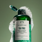 Green bottle of The Body Shop Tea Tree Skin Clearing Facial Wash with soap bubbles on a green background