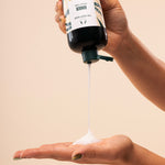 Hand holding a The Body Shop Ginger Conditioner with a beige background