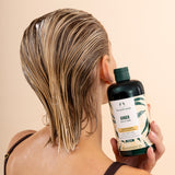 Person with wet hair holding a bottle of The Body Shop Ginger Conditioner against a beige background