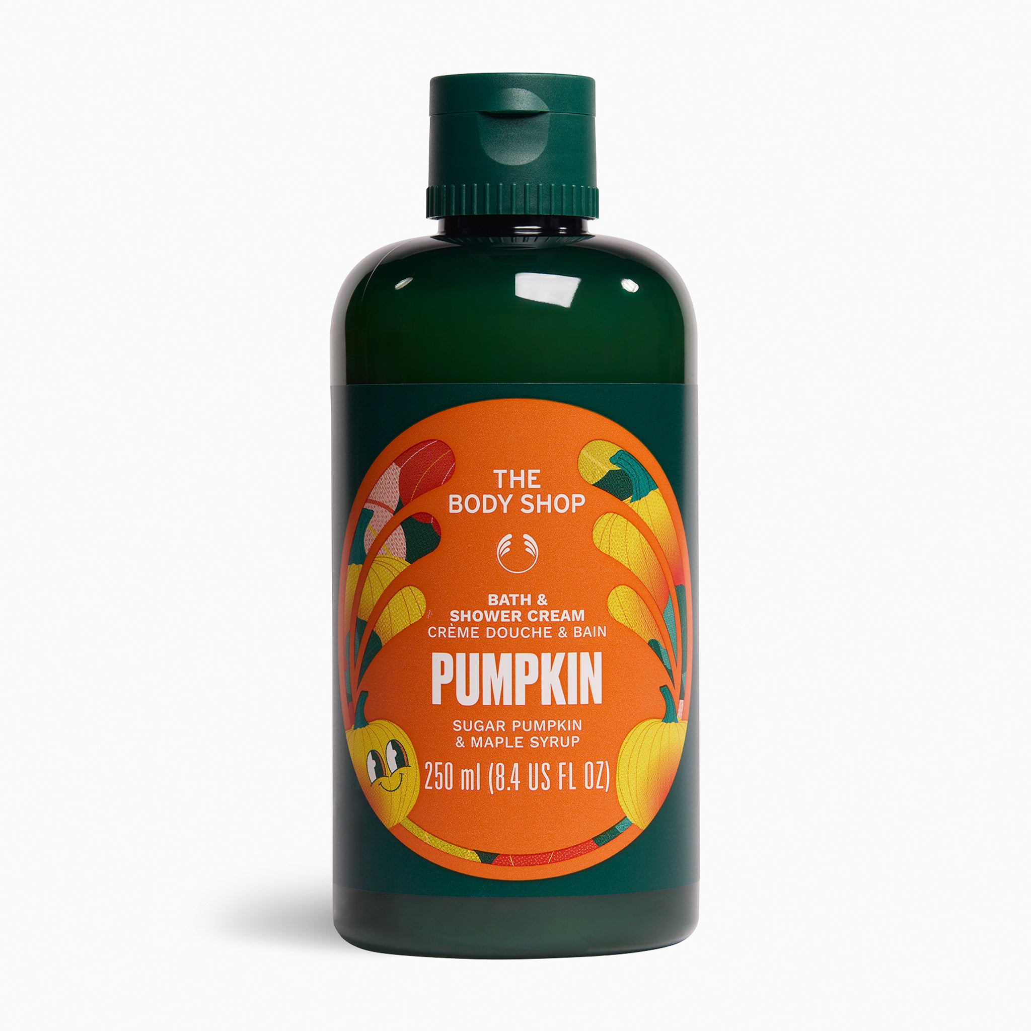 A 250 ml bottle of The Body Shop Pumpkin Bath & Shower Cream, featuring a dark green translucent bottle, a dark green flip-top cap, and a prominent orange circular label with illustrations of pumpkins and the brand name.