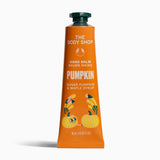 A squeeze tube of The Body Shop Hand Balm in the Pumpkin scent, featuring an orange body with white text and illustrations of pumpkins and leaves, topped with a dark green cap, set against a plain white background.