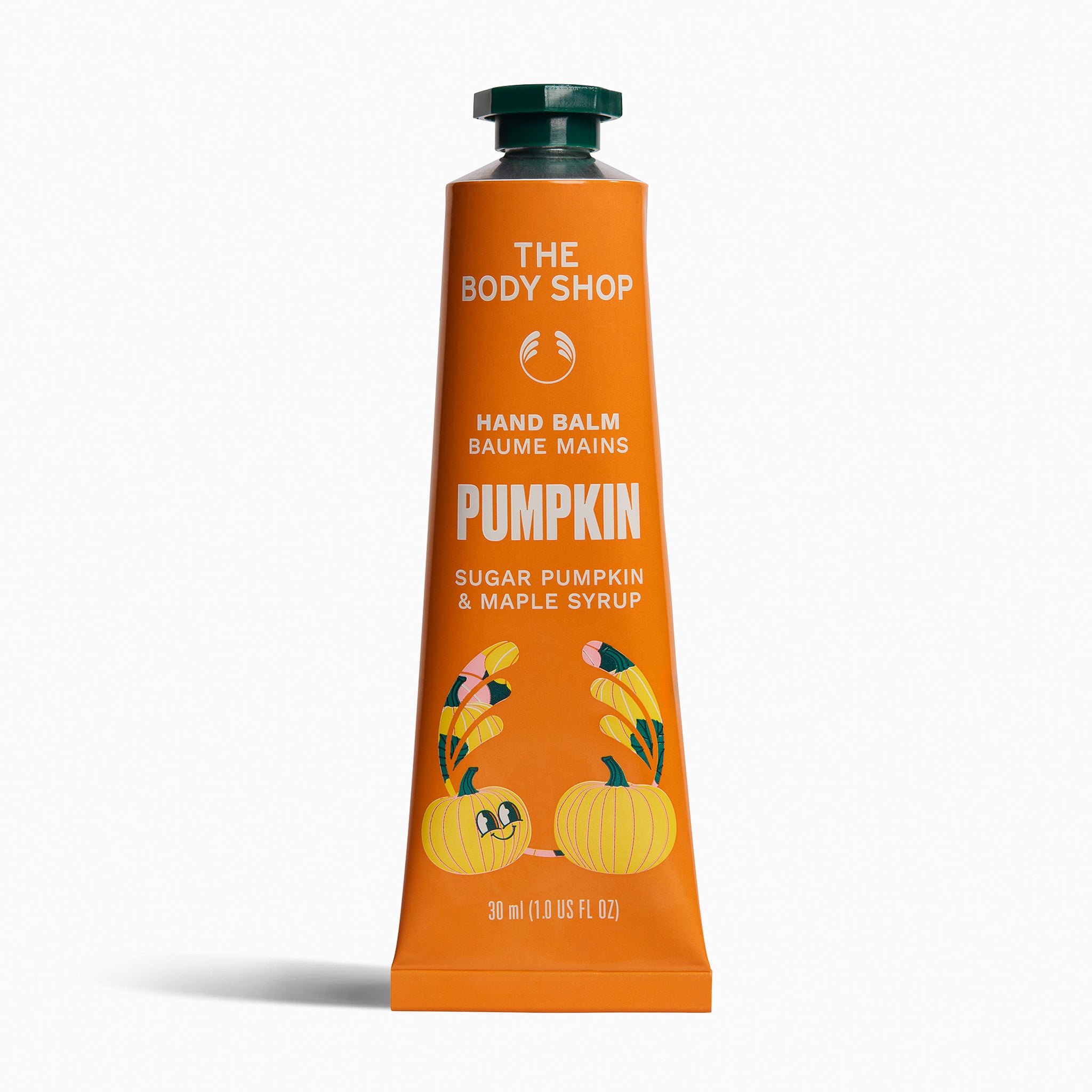 A squeeze tube of The Body Shop Hand Balm in the Pumpkin scent, featuring an orange body with white text and illustrations of pumpkins and leaves, topped with a dark green cap, set against a plain white background.
