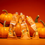 Three squeeze tubes of The Body Shop Pumpkin Hand Balm arranged in front of orange pumpkins on a warm orange background.