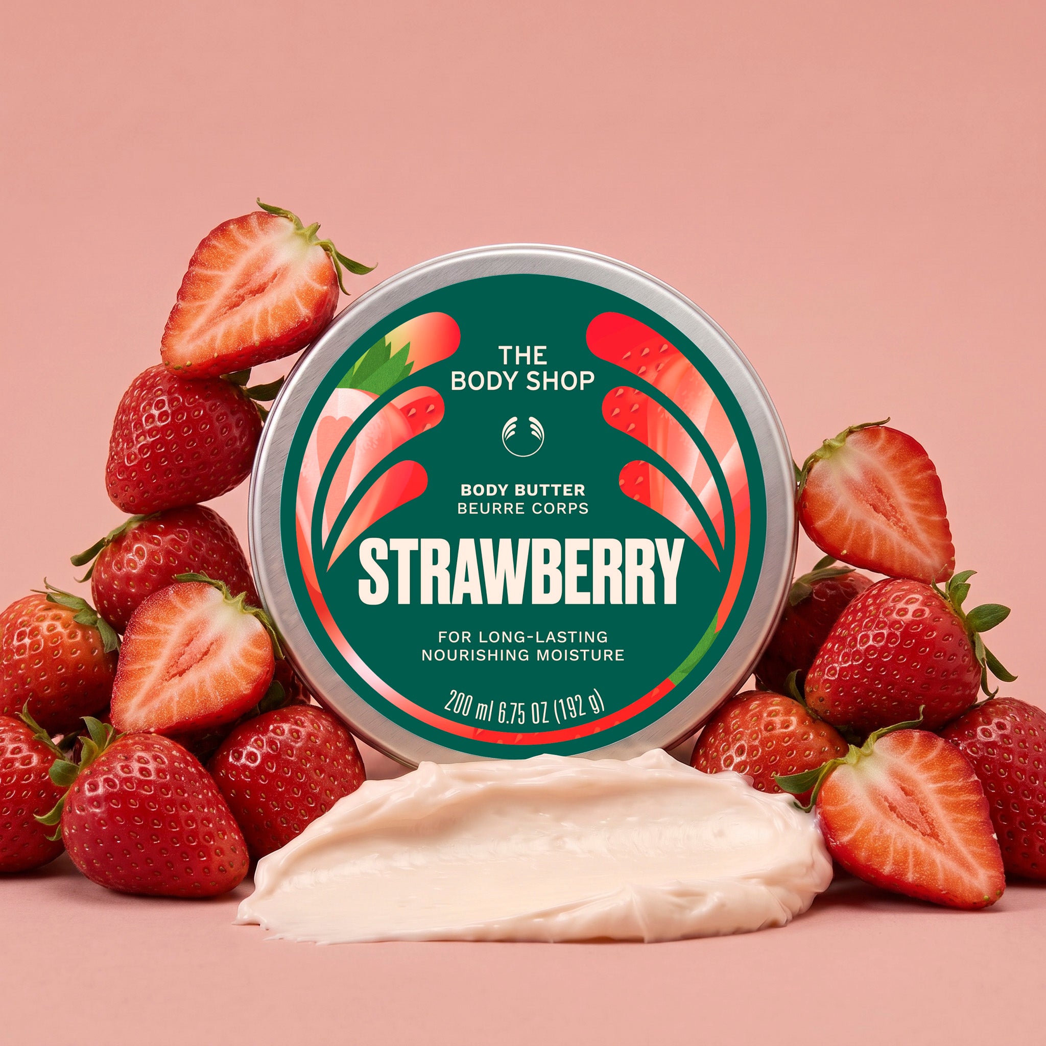 Strawberry body butter jar surrounded by strawberries, with a scoop of cream in front on a light pink background | The Body Shop