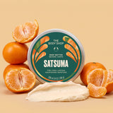 Satsuma body butter jar surrounded by satsumas, with a scoop of cream in front on a light orange background | The Body Shop