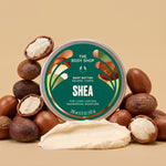 Shea body butter jar surrounded by coconuts, with a scoop of cream in front on a light brown background | The Body Shop
