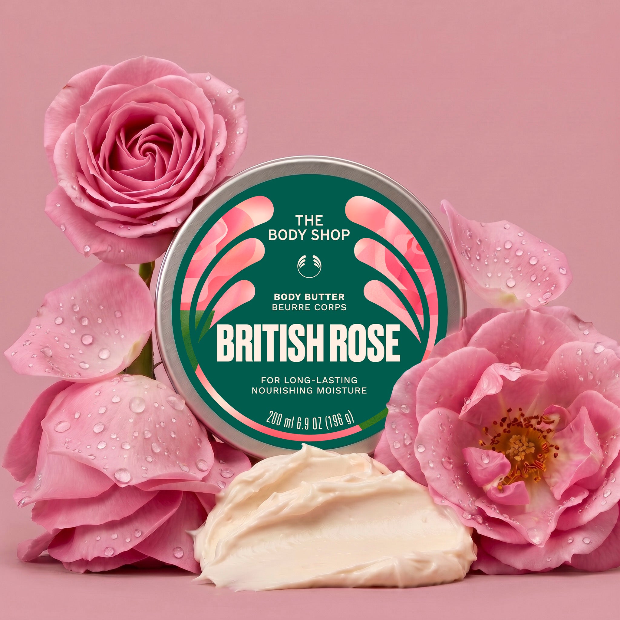 British Rose body butter jar surrounded by roses, with a scoop of cream in front on a pink background | The Body Shop
