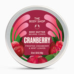 A round tin of The Body Shop Body Butter in Cranberry, featuring a metallic silver lid with a vibrant magenta and pink label decorated with illustrations of fresh cranberries and green mint leaves.