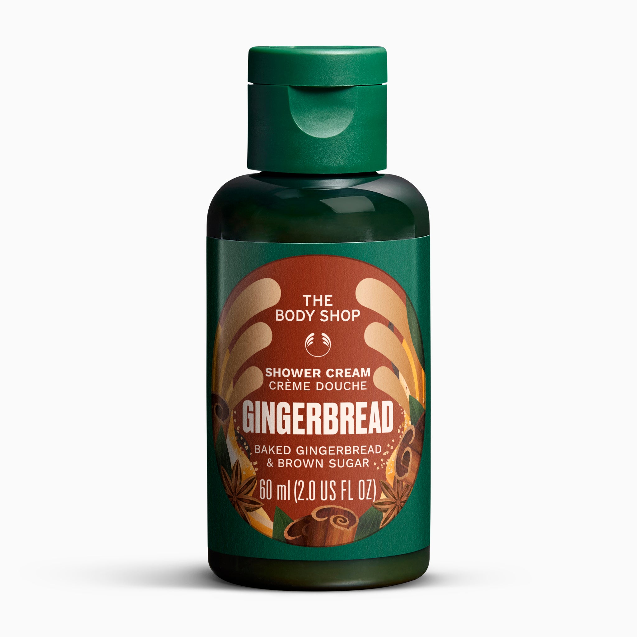 A 60 ml bottle of The Body Shop Gingerbread Shower Cream, featuring a dark green translucent bottle, a matching green flip-top cap, and a brown and orange label with illustrations of gingerbread and spices.