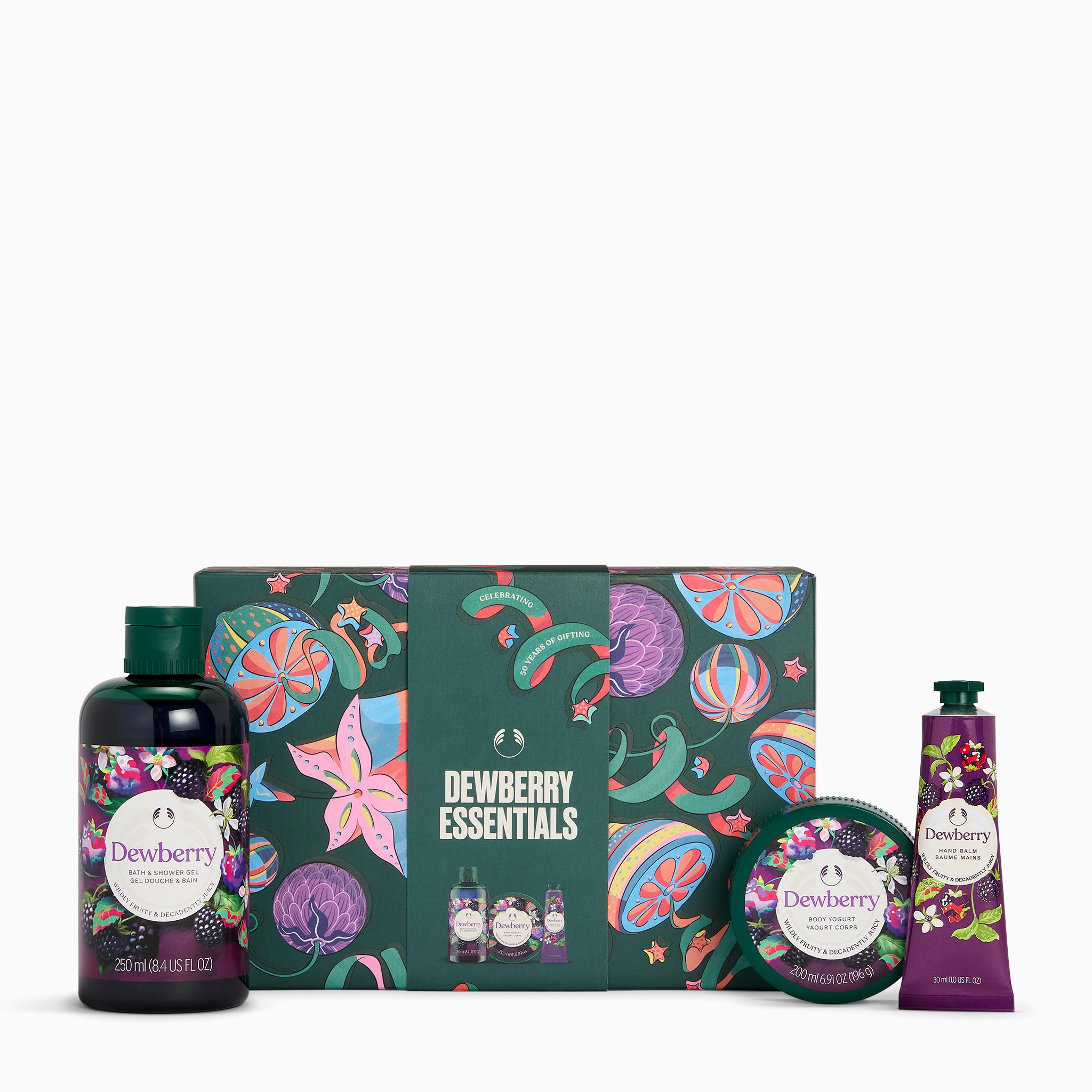 Thea Swann Dewberry Essentials gift set featuring a dark green patterned box, a large bottle of shower gel, a tube of hand cream, and a round tin of body butter, all decorated with colorful botanical illustrations.