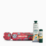 The Body Shop Hand & Lip Duo gift set featuring a red patterned cracker-style gift box, a tube of Hand Balm in Almond Milk, and a lip balm stick, arranged on a clean white background.