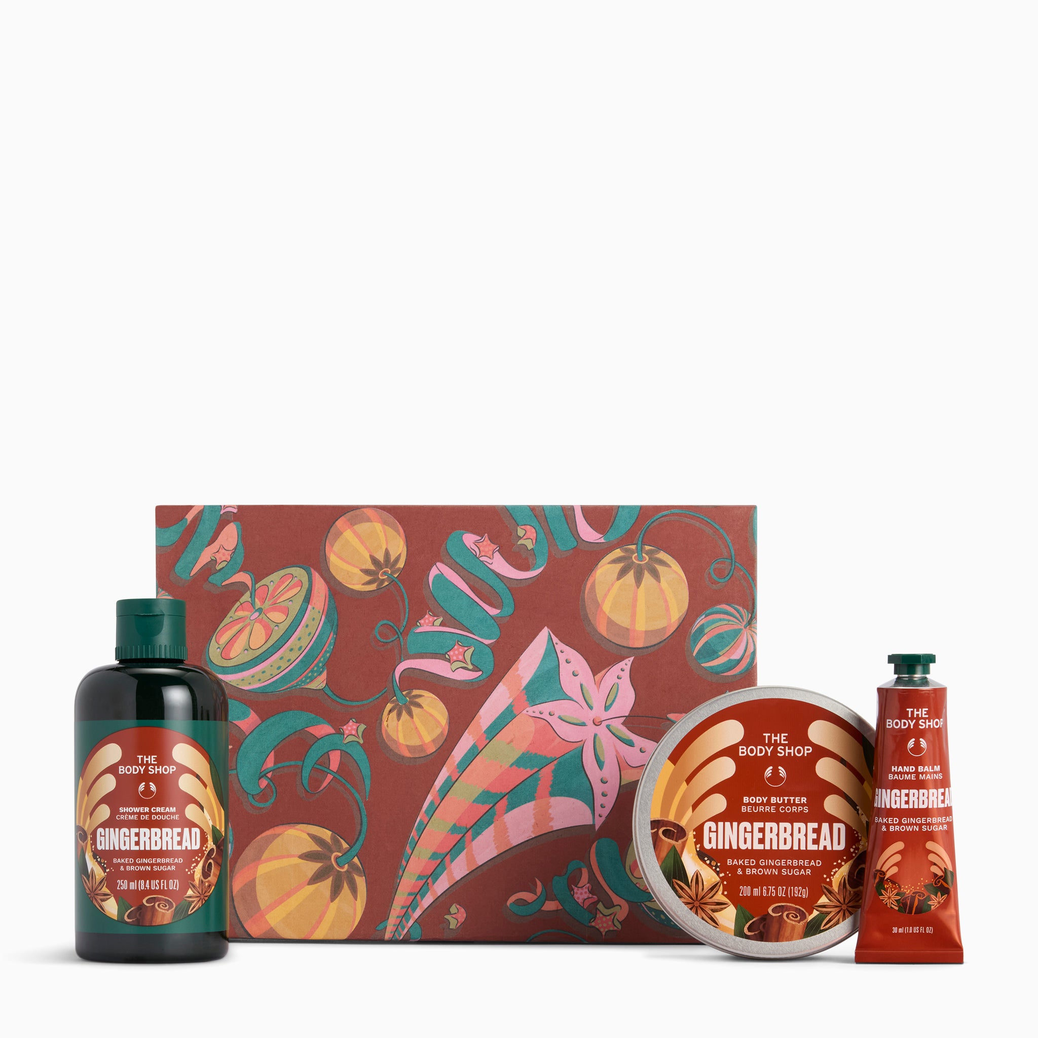 The Body Shop Gingerbread gift set featuring a dark amber bottle, a round tin, a tube, and a decorative gift box with a gingerbread-themed pattern, set against a plain white background.