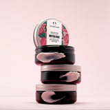 A stack of three The Body Shop British Rose Body Butter tubs with a pink background. 
