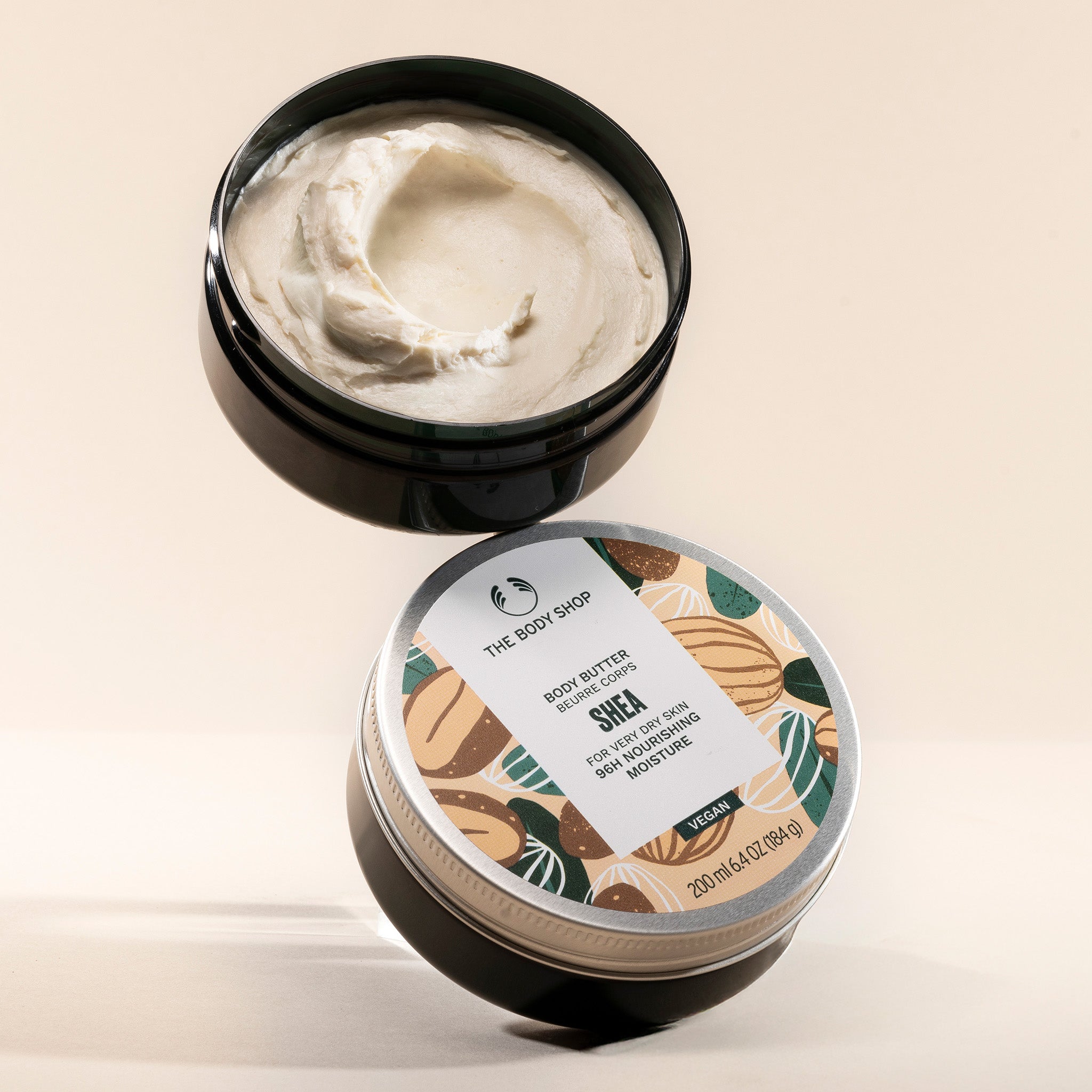 Shea body butter container with lid open on a beige background