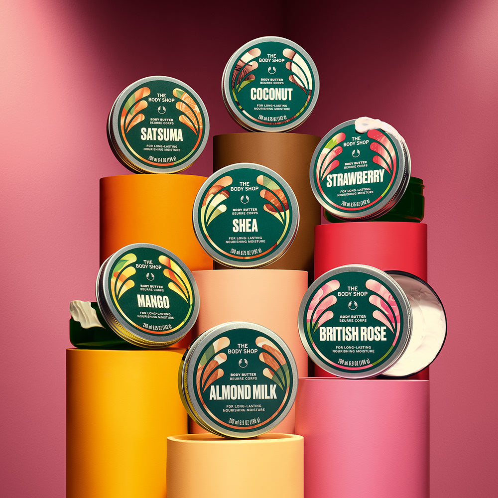 A collection of body butter jars arranged on bright cylindrical pedestals against a pink background | The Body Shop