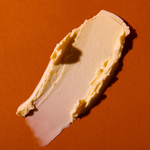 A thick smear of pale cream-colored cosmetic cream or balm on a solid orange background.