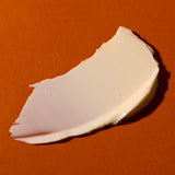 A thick, creamy off-white cosmetic or food smear on a solid orange background.