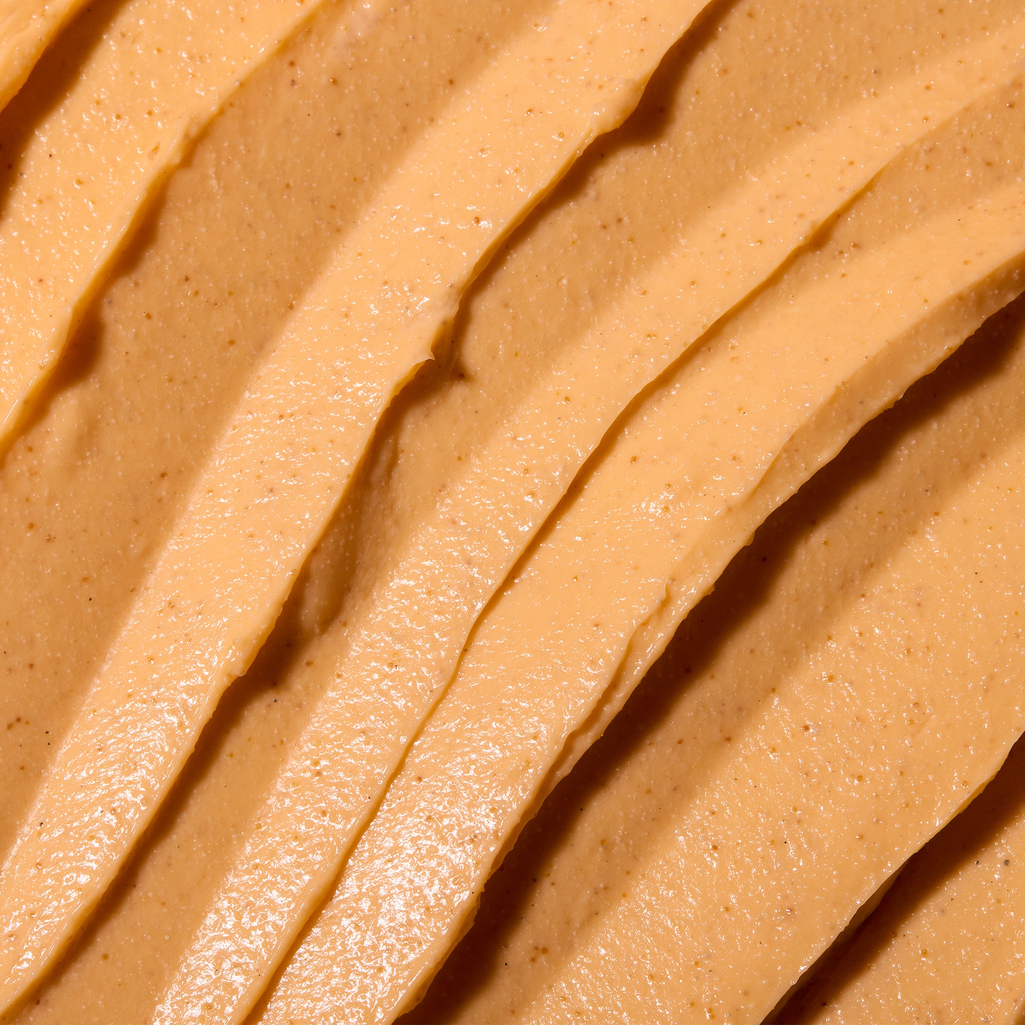 A close-up texture shot of a smooth, creamy peanut butter filling with diagonal ridges and a warm tan-brown color.