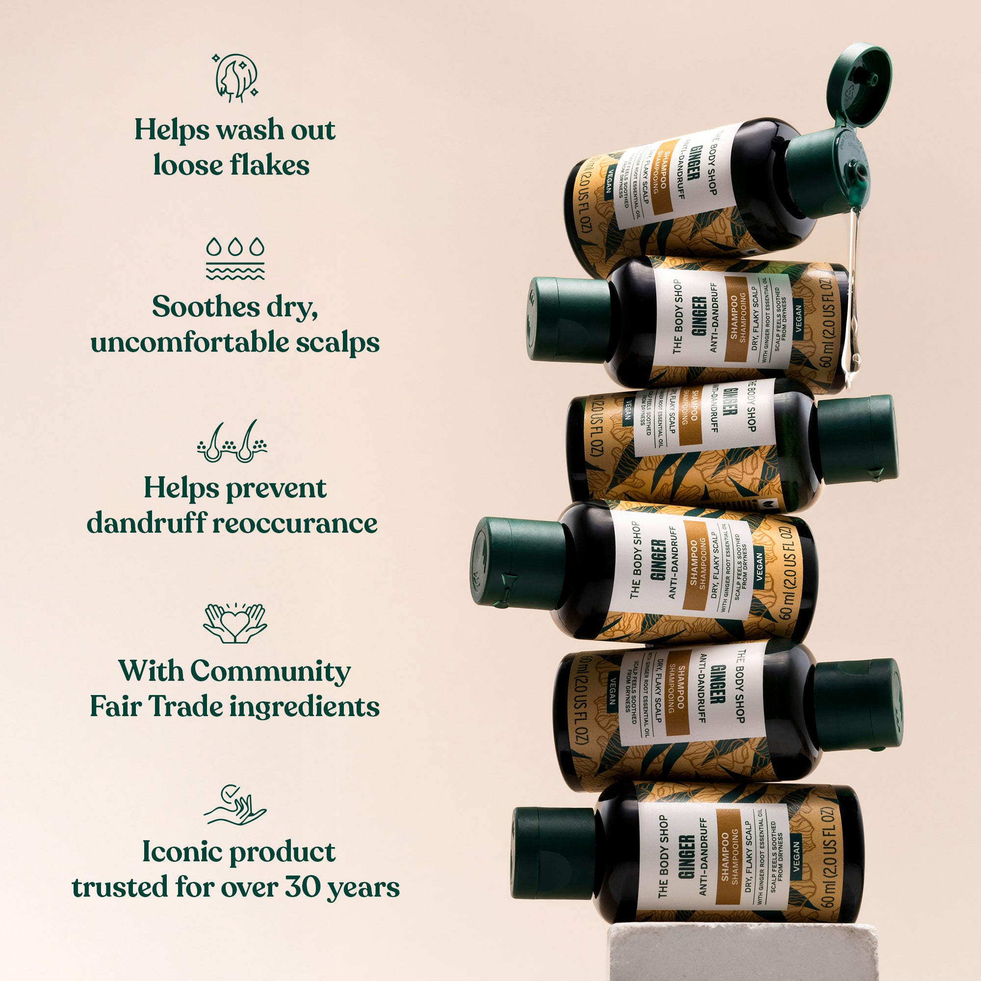 A stack of The Body Shop Ginger Shampoo bottles with a list of product benefits. Helps wash out loose flakes. Soothes dry, uncomfortable scalps. Helps prevent dandruff reoccurrence. With Community Fair Trade ingredients. Iconic product trusted for over 30 years.